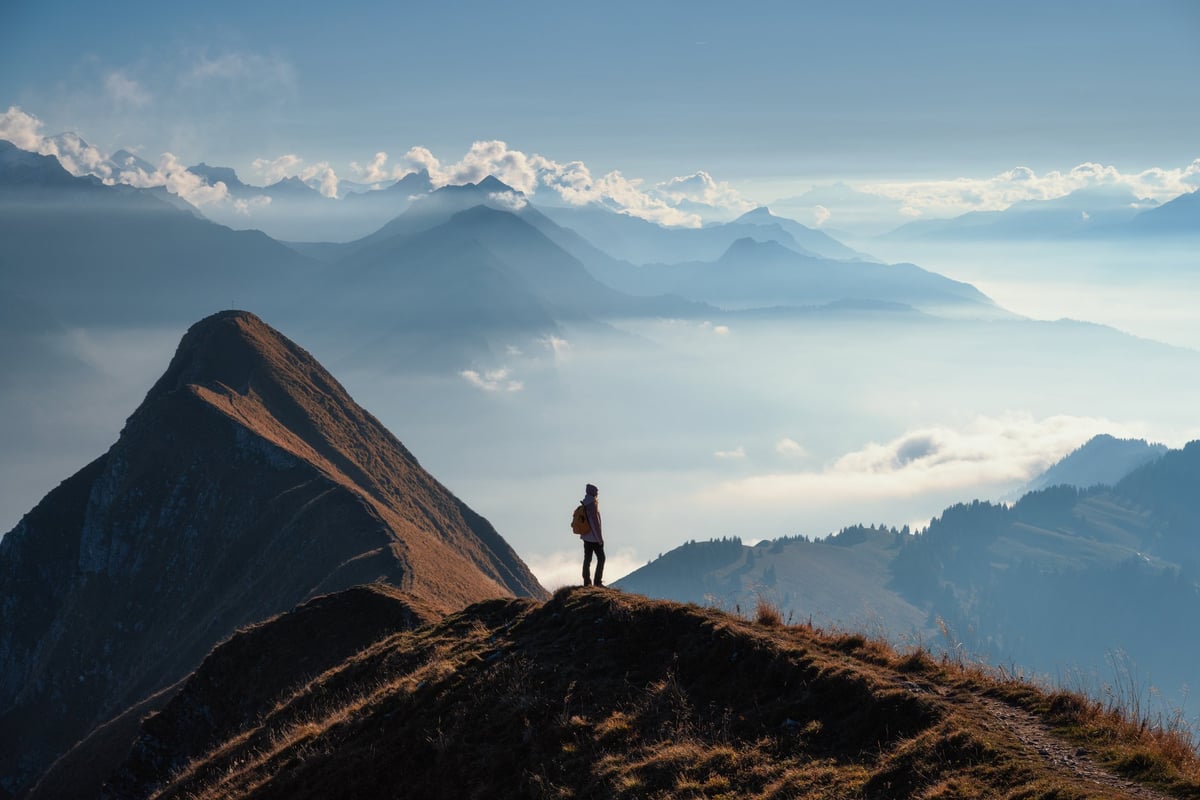 Woman with a backpack standing on a scenic mountain ridge at sunset