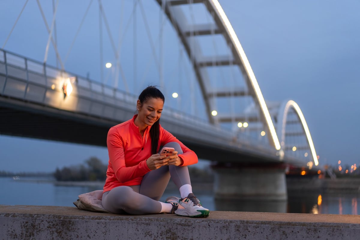 Young woman smiling at her phone after a workout outdoors at sunset